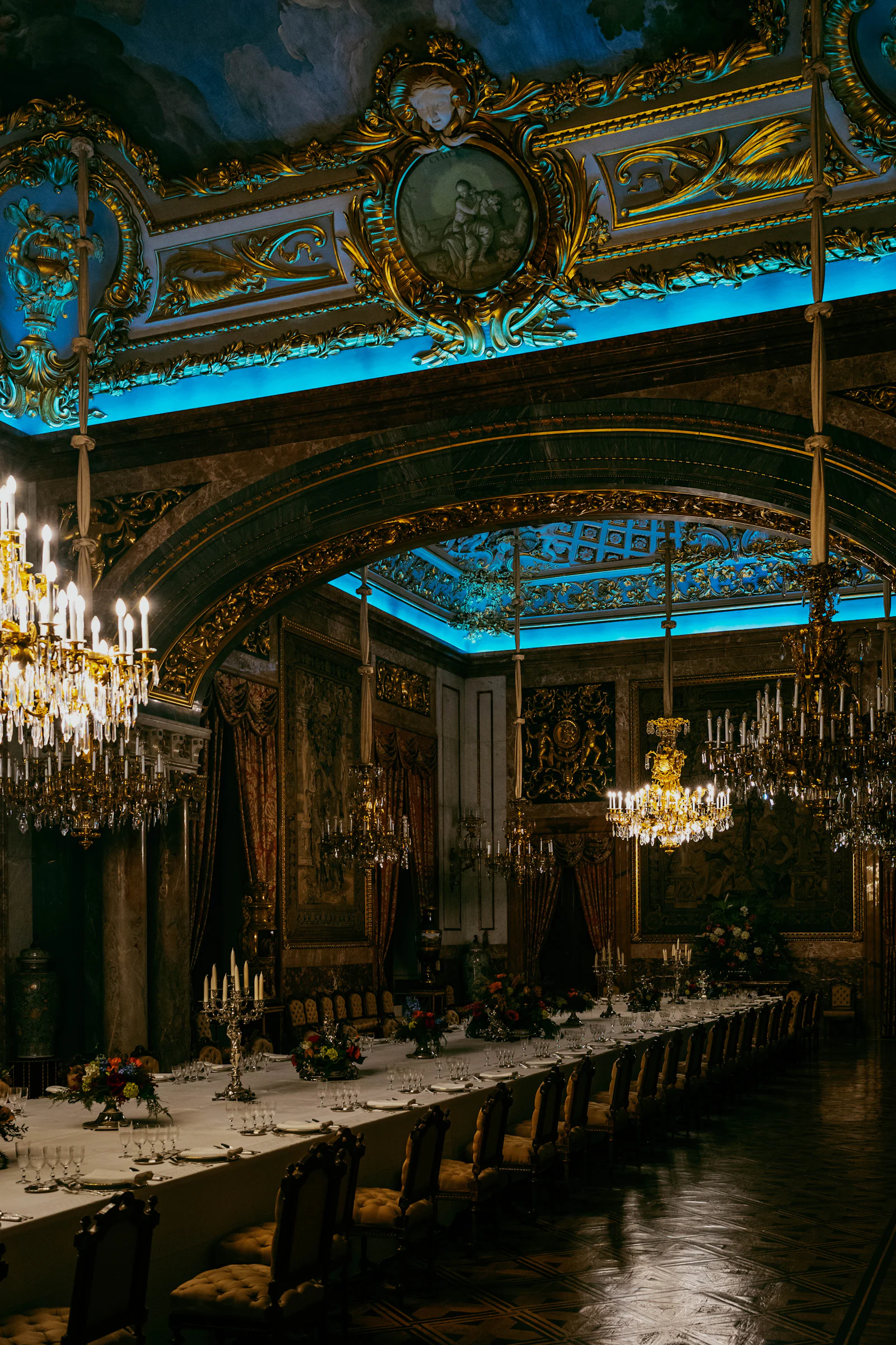 An opulent ballroom with chandeliers set for a formal dinner